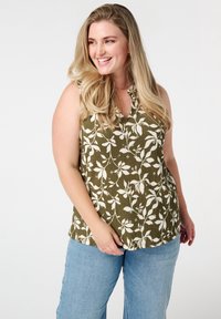 Olijfgroene mouwloze top met wit bloemenpatroon, v-hals ontwerp, gestructureerde stof, gecombineerd met lichtblauwe wijde jeans.