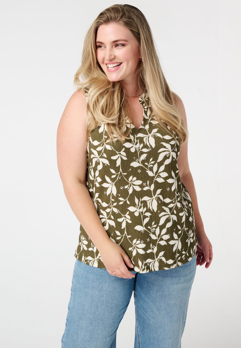 Haut sans manches vert olive avec un motif floral blanc, design en V, tissu texturé, associé à un jean large bleu clair.