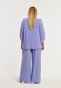 Lila tweedelig outfit met een losse, lange mouw top en wijde broek, gemaakt van zachte stof met een gladde textuur.