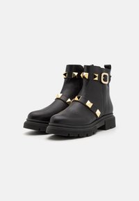 Botine negre din piele cu talpă groasă, decorate cu studuri piramidale aurii și o cataramă pe curea la glezne. Textură netedă, fermoar lateral.