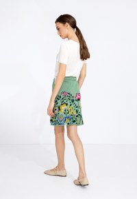 Jupe verte brodée avec des motifs floraux en rose, jaune et bleu. Présente une taille cintrée et une forme évasée. Associée à un haut blanc.