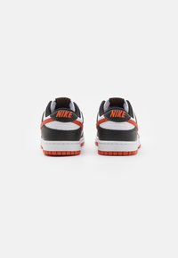 Baskets Nike noir et blanc avec des accents orange, présentant une tige texturée, un col rembourré et une semelle en caoutchouc avec un motif de bande de roulement.