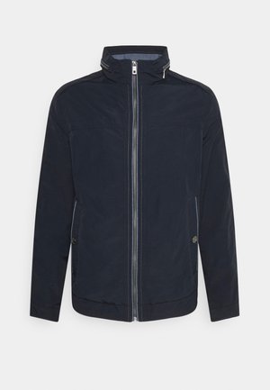 Pánská námořnicky modrá bunda s předním zipem, vysokým límcem a bočními kapsami na knoflíky, zobrazena na jednoduchém pozadí.