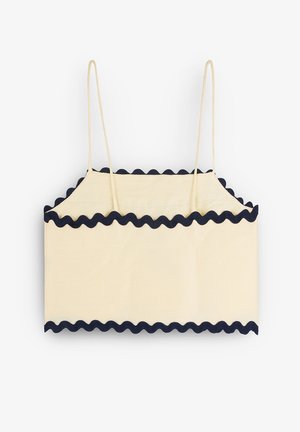 Top corto color crema con ribete en forma de concha en azul marino, que presenta tirantes finos y un diseño rectangular sencillo. Textura suave y tejido ligero.