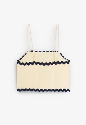Cream-colored crop top with navy scalloped trim, featuring thin straps and a simple rectangular design. Soft texture and lightweight fabric.