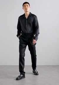 Sort satin langærmet skjorte med krave, parret med sorte bukser og polerede sorte sko, som skaber et monokromatisk look.