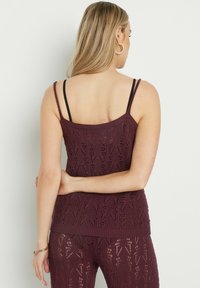 Burgunderröd stickad linne med spetsmönster, tunna axelband och ribbad nederkant, matchad med byxor. Texturen är lätt och andas.