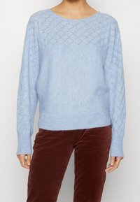 Jasnoniebieski sweter dzianinowy z diamentowym wzorem na rękawach i prążkowanym wykończeniem. Posiada długie rękawy i okrągły dekolt.