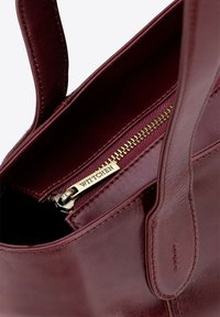 Bordeaux lederen handtas met dubbele handvatten, een binnenzak met rits en gouden hardware, en een gladde afwerking.