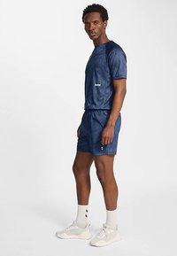 Marinblå sportset med kortärmad tröja i texturerat tyg, shorts med elastisk midja och vita logodetaljer. Modellen bär ljusa sneakers.