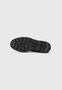 Semelle de botte en caoutchouc noir avec un motif de relief texturé, caractérisée par des rainures et des crêtes profondes conçues pour une adhérence et une stabilité optimales.