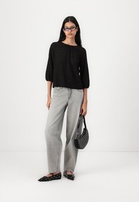 Black textured blouse with three-quarter sleeves, paired with light gray wide-leg jeans. Accessories include a small black bag with studs.