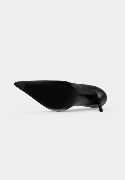 Chaussure noire à talon haut et bout pointu vue de dessous avec un talon fin sur un fond clair uni.