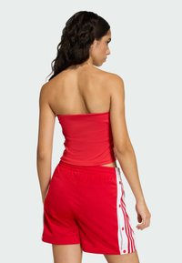 Červený top bez ramienok a červené šortky s bielymi bočnými pruhmi, so zapínaním na cvoky. Vyrobené z hladkej, elastickej tkaniny s priliehavým strihom.