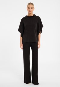 Schwarzes Strickoberteil mit einem entspannten, übergroßen Design und kurzen Ärmeln, kombiniert mit hoch taillierten, schwarzen Schlaghosen. Glatte Textur.