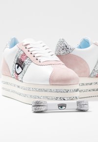 Plattform sneakers med vit och rosa mocka, glittriga detaljer, ögonmönster på sidan och texturerade vita snören med en matchande accessoar.