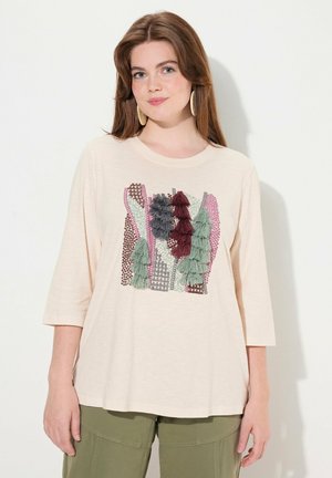 Camiseta de color beige claro con un cuello redondo, que presenta un colorido diseño bordado de árboles en verde, burdeos y rosa, con una textura suave.