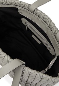 Sac en cuir gris en toile, avec une texture matelassée, doté d'un intérieur en tissu noir et d'une poche zippée. Deux poignées plates incluses.