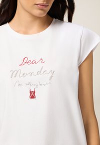 Camiseta de algodón blanca con texto bordado: "Querido lunes / No tengo nada que ponerme." Cuello redondeado y mangas cortas.