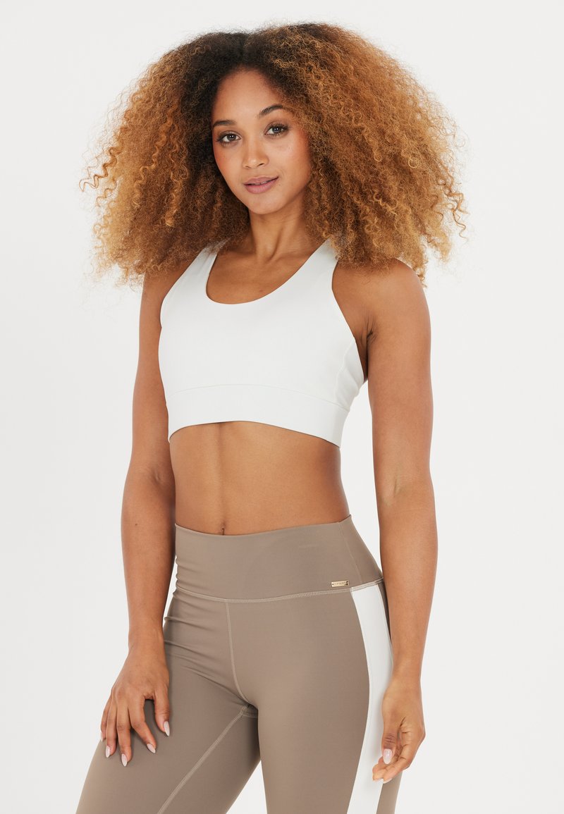 Soutien-gorge de sport gris clair avec un design court, doté d'une large bande et d'un décolleté en rond, associé à des leggings beiges taille haute avec des accents blancs.