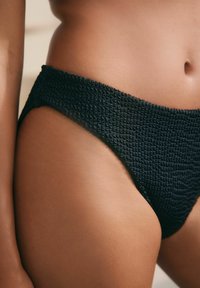 Costum de baie inferior texturat negru, cu un finisaj neted, având un design high-cut și material pliat pe talie.