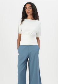 Witte kortek mouwtop met een verzamelde taille, gecombineerd met wijde blauwe broek. De stof lijkt soepel en lichtgewicht met minimale naden.