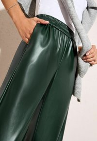 Zielone szerokie spodnie z sztucznej skóry z elastycznym pasem i bocznymi kieszeniami, stylizowane z jasnoszarym swetrem z dzianiny. Gładka, błyszcząca faktura.