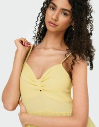 Robe jaune avec un design à l'avant torsadé, des bretelles fines et une jupe évasée. Fabriquée en tissu texturé, elle présente un matériau doux et fluide.