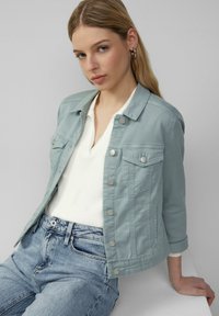 Lichtblauwe denim jas met een kraag, knopen aan de voorkant en twee borstzakken. Draag het over een witte ribbeltop en in combinatie met casual jeans.