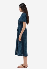 Abito midi blu navy con maniche corte, motivo floreale testurizzato, vita cintrata e gonna fluida, abbinato a sandali marroni.
