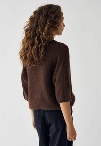 Rjav puhast pulover z ohlapnim krojem, raglan rokavi in rebrastimi manšetami, v kombinaciji s temnimi hlačami. Tekstura se zdi mehka in udobna.