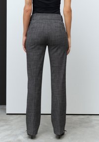 Pantaloni grigi a quadri su misura con vestibilità dritta, due tasche posteriori e una texture liscia. Le scarpe con tacco alto nere completano l'outfit.