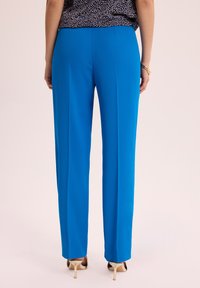 Niebieskie spodnie proste, wykonane z gładkiego materiału, z dopasowanym krojem i lekkimi zakładkami. Noszone z beżowymi szpilkami.