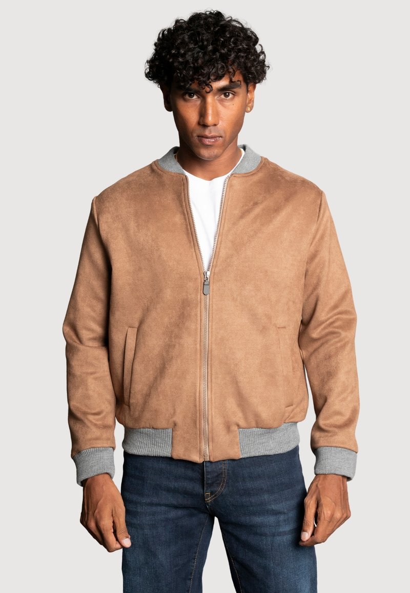 Veste en daim beige avec des poignets et un col côtelés gris, fermeture éclair à l'avant, deux poches latérales et une coupe décontractée. Assortie avec un jean foncé.