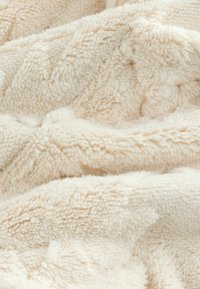 Lichtbeige pluche dekentje met een zachte, gestructureerde oppervlakte, gekenmerkt door een fluffy, diepe pool en subtiele golfpatronen overal.