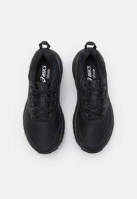 Chaussures de sport noires avec une tige en mesh texturé, une semelle rembourrée et un design à lacets. Présente un rabat en tissu au niveau du talon.