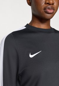 Μαύρο μπλουζάκι Nike με μακριά μανίκια, λευκές ρίγες στο πλάι και λογότυπο. Λείος υφασμάτινος κόμπος, γύρος λαιμός, προσαρμοσμένη εφαρμογή.