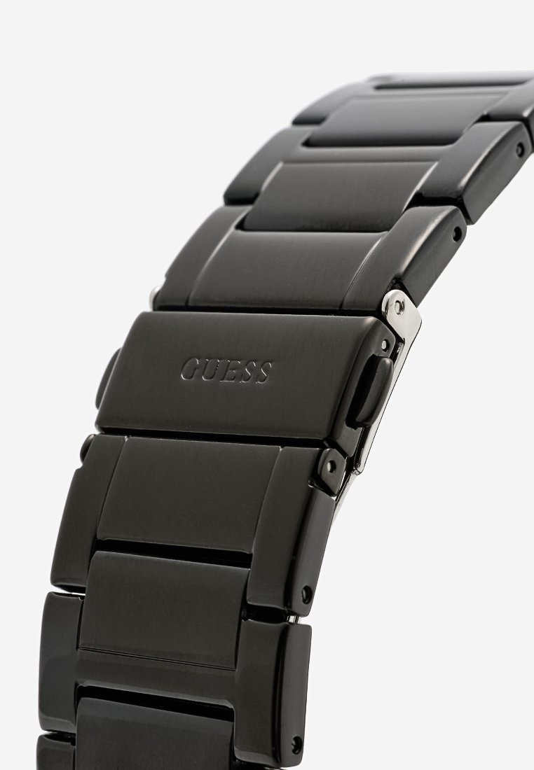 Czarny metalowy pasek do zegarka z prostokątnymi ogniwami, polerowaną powierzchnią, wygrawerowanym logo "GUESS" oraz srebrnym zapięciem.
