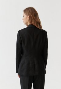 Černý přizpůsobený blazer z lnu, s robustní siluetou, klopovými límci a jedním rozParkem na zadní straně.