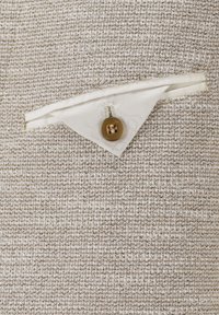 Hellbeige strukturierter Stoff mit einer kleinen dreieckigen Tasche, die mit einem beigen Futter versehen ist, und einem runden braunen Knopf, der befestigt ist.