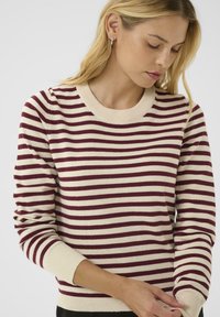 Pull en rayures aux couleurs bordeaux et crème, col rond côtelé, et tissu texturé, avec des manches longues et des poignets ajustés.