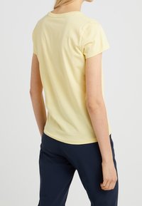 Gul bomullströja med korta ärmar, rundad halsringning och en figurnära passform. Slät textur, enkel design och inga synliga mönster.