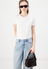 Λευκό κοντομάνικο T-shirt, ανοιχτό μπλε τζιν παντελόνι με ασημένιες λεπτομέρειες και μια μικρή σκούρα καφέ τσάντα με κοντό λουρί.