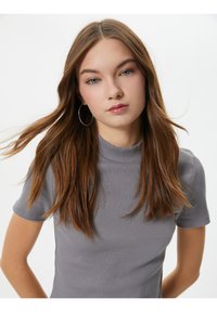 Grå ribbet t-shirt med høj halsudskæring og korte ærmer, der har en tætsiddende form og glat tekstur. Modellens hår dækker delvist skulderen.