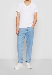 Pánské bílé tričko s véčkovým výstřihem, světle modré džíny rovného střihu, bílé tenisky na ploché podrážce. Jednoduchý design, měkký bavlněný materiál, volný střih.