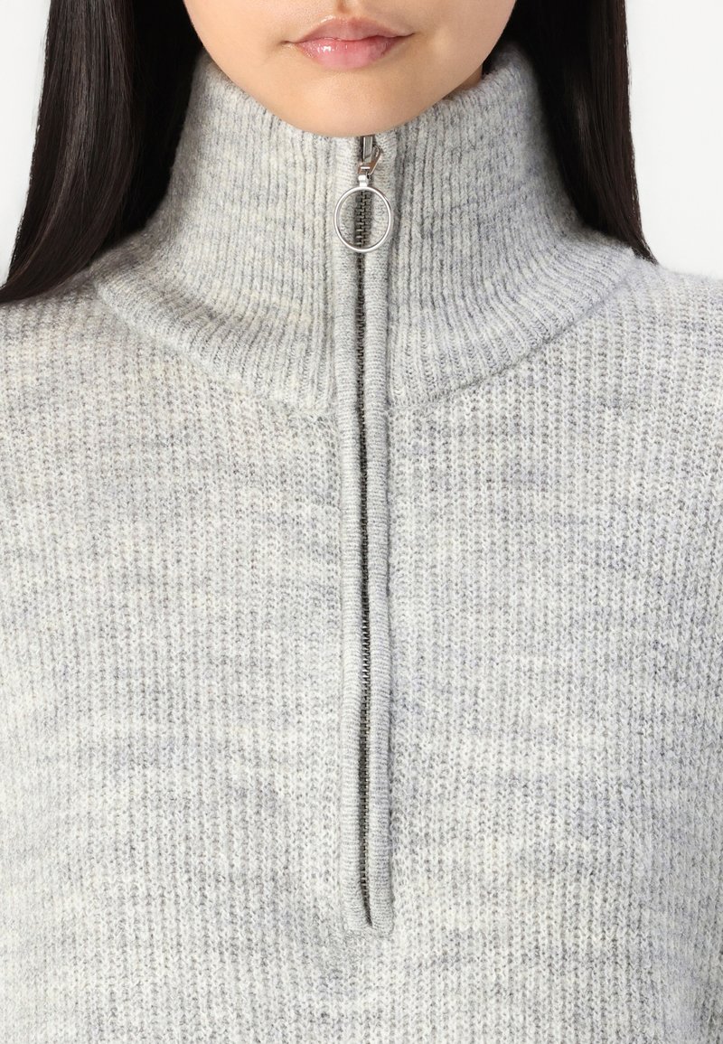 Szary sweter dziany z wysokim kołnierzem i zamkiem błyskawicznym z okrągłym uchwytem. Tekstura jest miękka, z delikatnym wzorem.