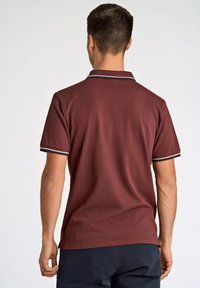 Bordowa koszulka polo z klasycznym kołnierzem, krótkimi rękawami oraz kontrastowymi ciemnymi i jasnymi paskami na mankietach i kołnierzu.