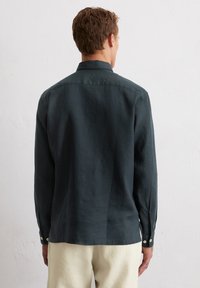 Chemise à manches longues, verte foncée, avec un col, au design simple et à la coupe décontractée. Fabriquée en tissu léger.