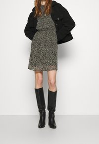 Robe noire à fleurs avec des manches courtes, taille cintrée et jupe évasée, associée à des bottes en cuir noires jusqu'aux genoux et une veste noire.