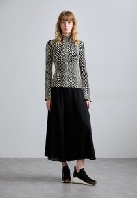 Top a righe bianche e nere con maniche lunghe abbinato a una gonna nera fluida a pieghe e sneakers nere con dettagli leopardati.